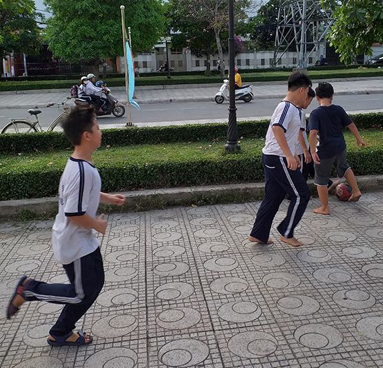 Trẻ đá bóng ở vườn hoa ven đường