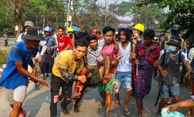 Một người đàn ông được đưa đến nơi an toàn sau khi bị bắn trong cuộc biểu tình ở Yangon ngày 14.3 /// Ảnh: AFP