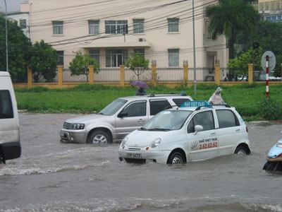 Đường Xuân Thủy-Cầu Giấy như một khúc sông giữa phố (Ảnh: Sông Lam)  (Dân trí) - Xe buýt bỏ trạm, taxi từ chối chở khách, xe ôm ép giá, dịch vụ sửa xe chết máy đắt khách, đó là những hình ảnh Dân trí ghi được trong trận mưa “thế kỷ”, kéo dài đã 2 ngày tại Hà Nội. Trường học và công sở hôm nay cũng vắng hoe…  >>  Hà Nội “tê liệt” trong trận mưa cực lớn  >>  Chùm ảnh: Bì bõm giữa “biển nước” Hà Nội  >> Hàng loạt chuyến bay không thể hạ cánh xuống Nội Bài  Xe buýt bỏ trạm, xe ôm ép giá…  Con đường Phạm Hùng nếu không có những dòng xe ì à ì ạch nối đuôi nhau thì chẳng ai còn nhận ra đây là đường hay là… sông nữa. Cả một đoạn đường dài ngập sâu trong nước, có đoạn ngập gần 1m. Đoạn đường Phạm Hùng - Khuất Duy Tiến nối ra đường Nguyễn Trãi đang tiến hành thi công, nước ngập sâu trong bùn lầy nên hàng loạt chiếc xe chết máy và phải dắt bộ. Thậm chí, những chiếc taxi liều lĩnh phóng qua “bể bơi giữa đường phố” như cách gọi của cánh tài xế, lập tức từ “xe taxi” trở thành “thuyền taxi” nổi lềnh bềnh trên mặt nước rồi chết máy.   Xe taxi trôi lềnh bềnh trên đường Xuân Thủy-Cầu Giấy  Cũng vì ngấm đòn nên các xe taxi 4 chỗ ngồi đều từ chối chở khách, dù khách sẵn sàng trả giá cao gấp đôi, thậm chí gấp 3 so với giá thường ngày. Chị Mỹ Dung, đứng đón xe taxi ở đường Phạm Hùng than thở: “Sáng nay có việc đi gấp qua khu vực Ba Đình, mình kêu 3 chiếc taxi rồi mà chẳng có tài xế nào chịu chở. Đúng là nhìn đường biến thành sông đã ngán rồi, huống hồ còn phải vật lộn với tắc đường, nghẽn xe”.  Taxi không chịu chở khách, cánh xe ôm cũng “làm cao” không kém. Chỉ giúp chở chị Dung từ lề đường bên này sang lề đường bên kia của đường Phạm Hùng - đoạn đường sau một đêm mưa bỗng biến thành sông - bác tài đã hét giá 10.000 đồng mà chị Dung cũng phải đi khi tay xách nách mang đồ đạc lỉnh kỉnh. Và từ Phạm Hùng về bến xe buýt trung gian ở Kim Mã-Cầu Giấy, bác tài cũng “xin” của chị Dung 50.000 đồng, mà nếu như ngày thường chỉ cần 10.000 đồng thì một đám xe ôm đã xúm lại.   Nhiều tuyến đường trở thành “dòng sông lớn” gây ách tắc giao thông  Theo ghi nhận của Dân trí, nhiều tuyến giao thông ở Hà Nội rơi vào cảnh tắc nghẽn nghiêm trọng, thậm chí là đường một chiều như đường Nguyễn Thái Học cũng tắc. Nguyên nhân tắc đường do có những đoạn nước ngập sâu khiến nhiều xe chết máy.  Dịch vụ sửa xe chết máy, thông bugi trở nên đắt khách hơn bao giờ hết. Anh Tuấn, một chủ tiệm sửa xe máy trên đường Nguyễn Thái Học phấn khởi nói: “Nhờ đường ngập mà sáng giờ mình đã bán được hơn 30 chiếc bugi cho khách hàng, xe qua đoạn này đều chết máy, thoáng một cái đã hết hàng sửa cho khách”.   Xe máy chết máy, xe tải cũng “ngủm” vì đường ngập sâu trong nước  Trên nhiều tuyến đường, Công ty cấp thoát nước thành phố đã cho mở nhiều miệng cống nhằm tăng lưu lượng thoát nước. Tuy nhiên, cách làm này chỉ được xem như “muối bỏ biển”, bởi lượng mưa quá to. “Cứ mưa to là ngập, đường càng hiện đại ngập càng to, không biết bao giờ Hà Nội mới thoát cảnh “lội lụt” trên đường phố thế này”, bác Nguyễn Văn Sỹ, một cán bộ công chức đã về hưu than thở.   Mở miệng cống thoát nước để cấp cứu nhưng không lại.  Công sở vắng bóng, trường học… vắng teo  Mưa lớn ngập lụt các đường phố cũng chính là nguyên nhân khiến các công sở vắng bóng nhân viên. Anh Hoàng Hà, sếp của một cơ quan nhà nước nói: “Sáng nay mở mail ra mình nhận được một loạt đơn xin nghỉ làm của nhân viên vì đường… ngập. Không cho nghỉ cũng không được, nhưng công việc của cơ quan vì thế mà cũng đình trệ hẳn”.  Chị Mai Hà, làm ở công ty về dược phẩm thì bảo, sáng nay chị dắt xe ra đến ngõ mà nước ngập sâu quá nên lại quay vào nhà, đến khoảng 11h khi mưa đã ngớt chị lại liều phóng xe đến công sở để xử lý công việc. “Hóa ra công ty cũng lác đác có vài người đi làm, còn lại đều xin nghỉ”, chị Hà cho hay.  Chị Lan Anh, ở chung cư CT5, đường Phạm Hùng thì không mỗi mình chị nghỉ làm mà cả 2 đứa con - một đứa học mẫu giáo và một đứa học cấp 2 - cũng nghỉ. “Cô giáo của cháu điện thoại bảo xin nghỉ vì đường ngập không đi được. Mà nếu cô giáo có đến thì cũng chẳng có mấy học sinh đi học đâu”, chị Lan Anh khẳng định.  Các trường học tại Hà Nội hầu như vắng teo học sinh, sinh viên. Sinh viên Nguyễn Thị Hải, Phân viện Báo chí và tuyên truyền Hà Nội nói: “Lớp mình gần 50 người mà giờ có mười mấy người đến lớp, thầy giáo đến lớp cũng trễ hơn nửa tiếng vì tắc đường. Hai tiết cuối thì được nghỉ luôn vì thầy giáo không đến dạy được”.  Điểm đáng chú ý là, học sinh, sinh viên không đến trường được vì nhiều xe buýt bỏ trạm vì đường ngập. Sinh viên Nguyễn Thị Hà, đứng chờ xe buýt trên tuyến đường Xuân Thủy - Cầu Giấy cho biết: “Mình đứng từ 7h sáng mà đến 9h vẫn không một chiếc xe buýt nào đỗ vào đón khách. Xe máy không có, xe taxi thì không dám mơ, xe buýt lại không chở, sáng nay xem như nghỉ học”.   Xe buýt không ghé trạm khiến học sinh, sinh viên “sống dở, chết dở”  Nhiều sinh viên may mắn hơn khi lên được xe buýt, thì lại phải cuốc bộ một đoạn đường dài. Minh Đức, sinh viên Trường đại học Khoa học tự nhiên - ĐH Quốc gia Hà Nội than thở: “Chưa khi nào thê thảm như hôm nay khi cuốc bộ hơn 1km trong nước để đến lớp. Khổ nhất là mỗi chiếc xe máy, xe ô tô cứ đi ngang qua là té nước như mưa vào người, ướt hết cả áo quần, sách vở”.  Xe taxi trôi lềnh bềnh trên đường Xuân Thủy-Cầu Giấy