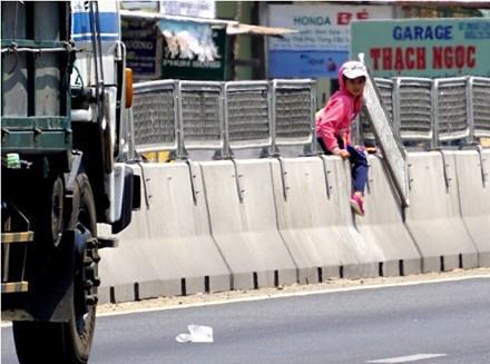 Một em học sinh tiểu học đang leo qua dải phân cách, ở vị trí lưới chống lóa bị tháo gỡ.